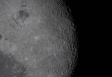 A detailed view of the moon surface showing a rugged lunar landscape pockmarked with craters under stark sunlight.
