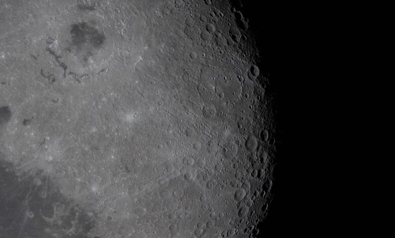 A detailed view of the moon surface showing a rugged lunar landscape pockmarked with craters under stark sunlight.