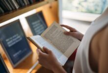 A person reading an open book among the shelves of a library