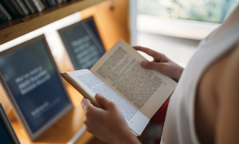 A person reading an open book among the shelves of a library